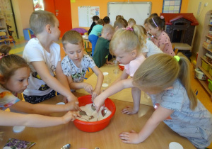 Dzieci nabierają łyżkami sól z miski.